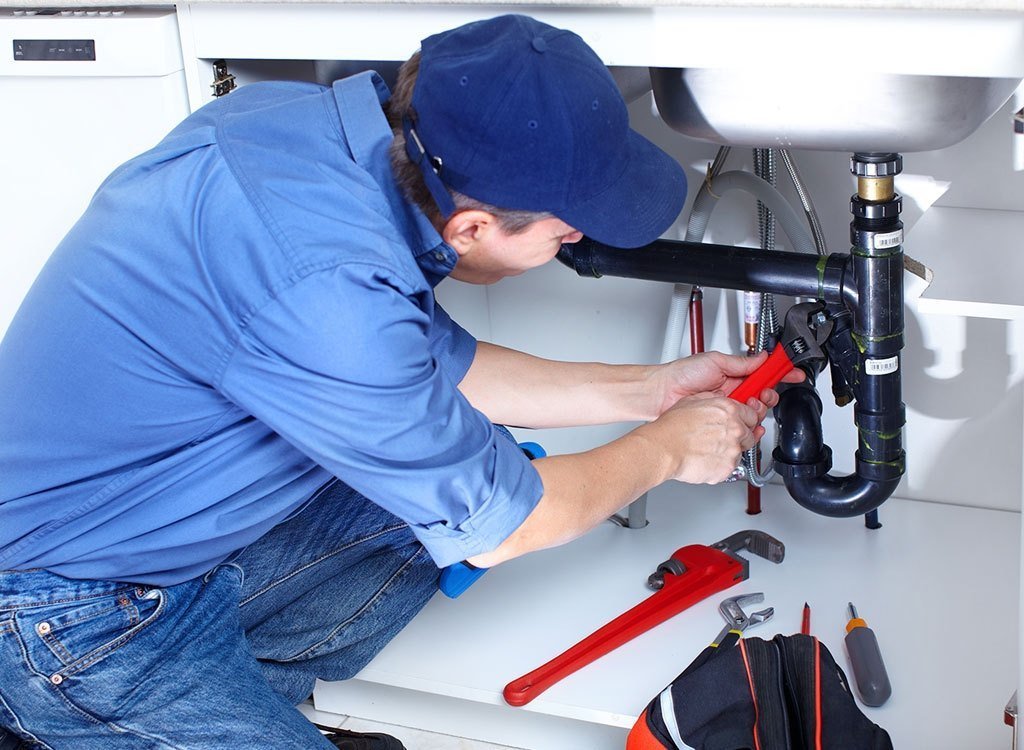 Plumber repairing pipework under a sink